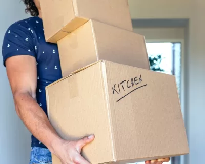 A close up of 3 cardboard moving boxes being carried by a man in a blue shirt.
