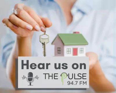A woman holds a small model house in one hand and a house key in the other. The words say 'Hear us on The Pulse 94.7 FM'.
